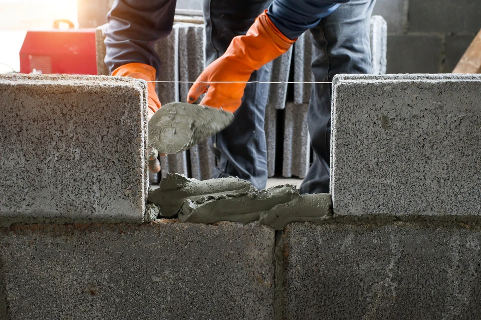 Chantier de construction en extérieur avec ouvrier appliquant mortier entre blocs de béton cellulaire pour édification d'un mur