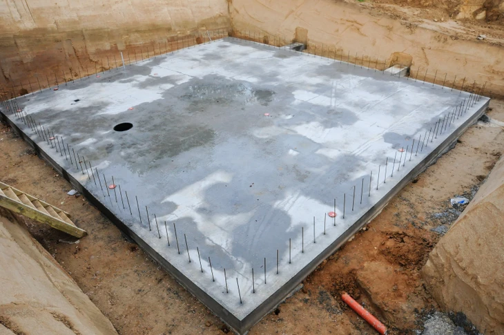Chantier de construction résidentielle avec dalle béton fraîchement coulée au premier plan et maisons individuelles en briques en arrière-plan