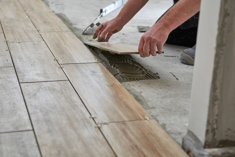 Artisan posant du carrelage gris anthracite sur chape ciment avec adhésif